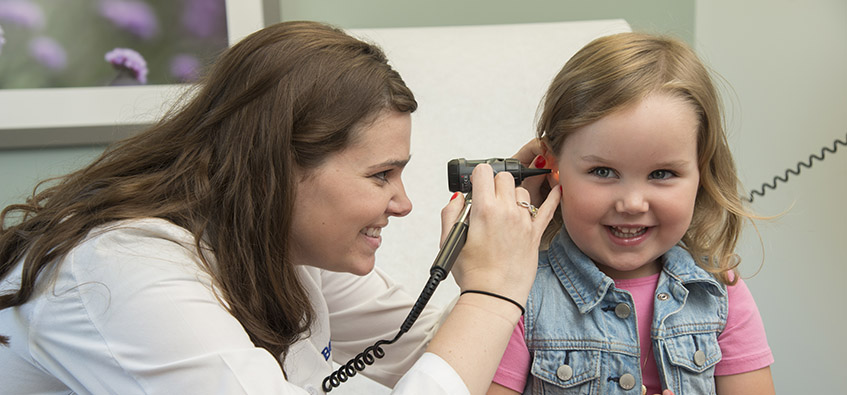 Family medicine doctor uses otoscope to examine ear of young girl