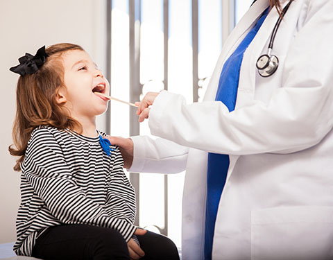 Little girl opens mouth while pediatrician examines